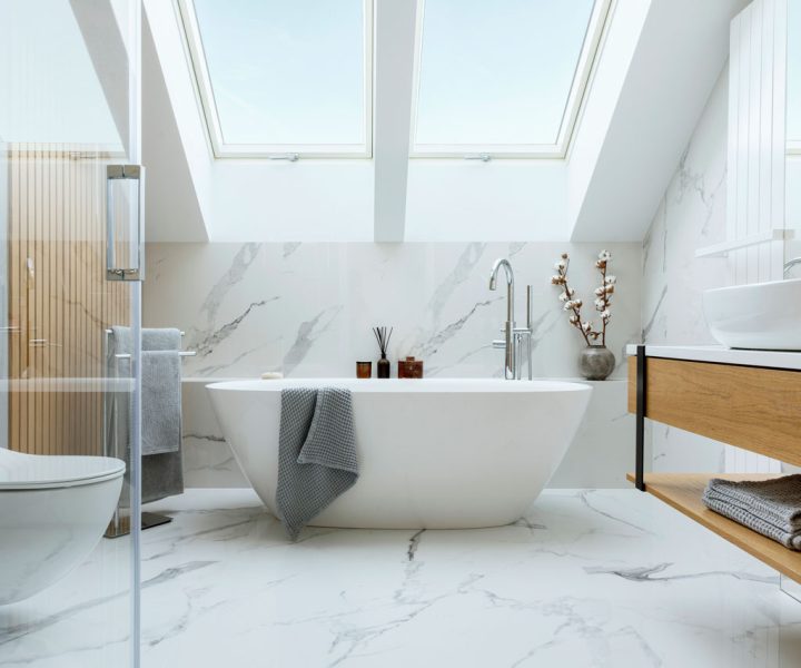 A luxurious bathroom featuring a freestanding bathtub, marble walls and flooring, and large skylights that allow natural light to flood the space. The design includes a wooden vanity, a glass shower enclosure, and decorative elements like candles and plants.