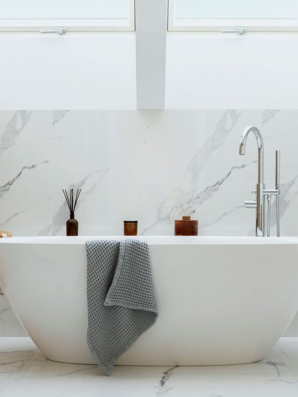 A sophisticated bathroom with a freestanding bathtub, marble walls and flooring, and large skylights. The design includes a wooden vanity, a glass shower enclosure, and decorative accents such as candles and towels.